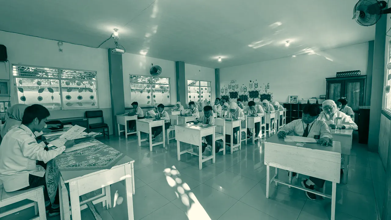 Ruang kelas dengan deretan meja belajar dan pelajar berseragam.