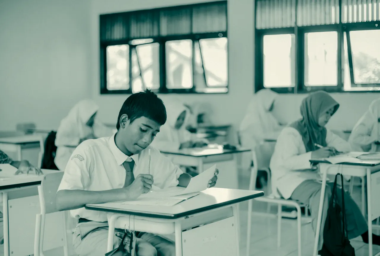 Seorang pelajar berseragam menulis di buku tulis di meja kelas.